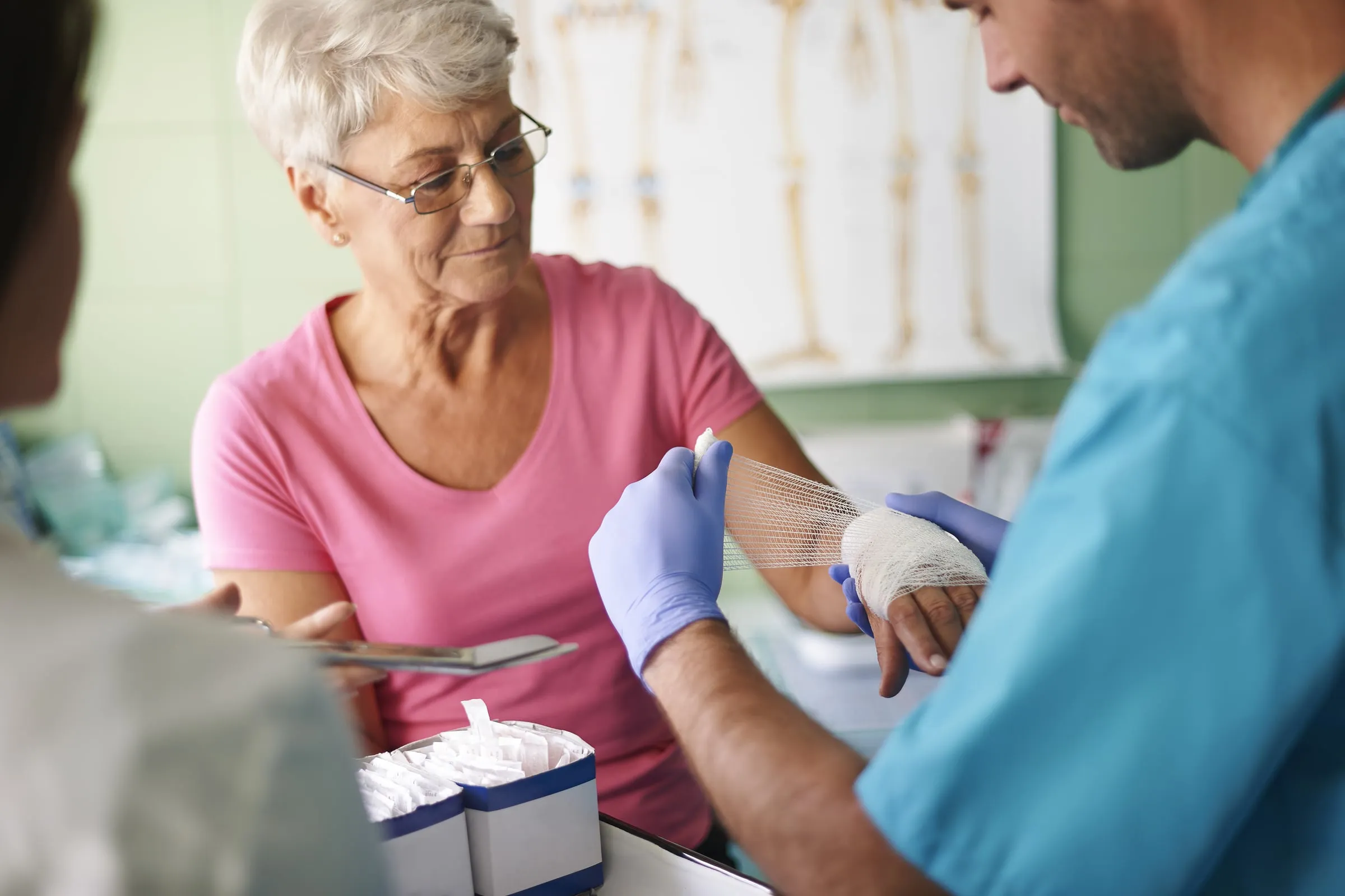 A nurse in gloves bandaging the hand of an older woman